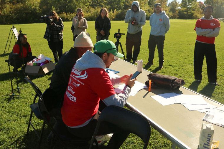 Volunteer at a table on the lawn with camera crew behind