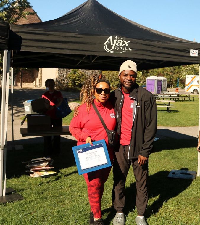 Two friends holding the Mayor's certificate under the Ajax tent